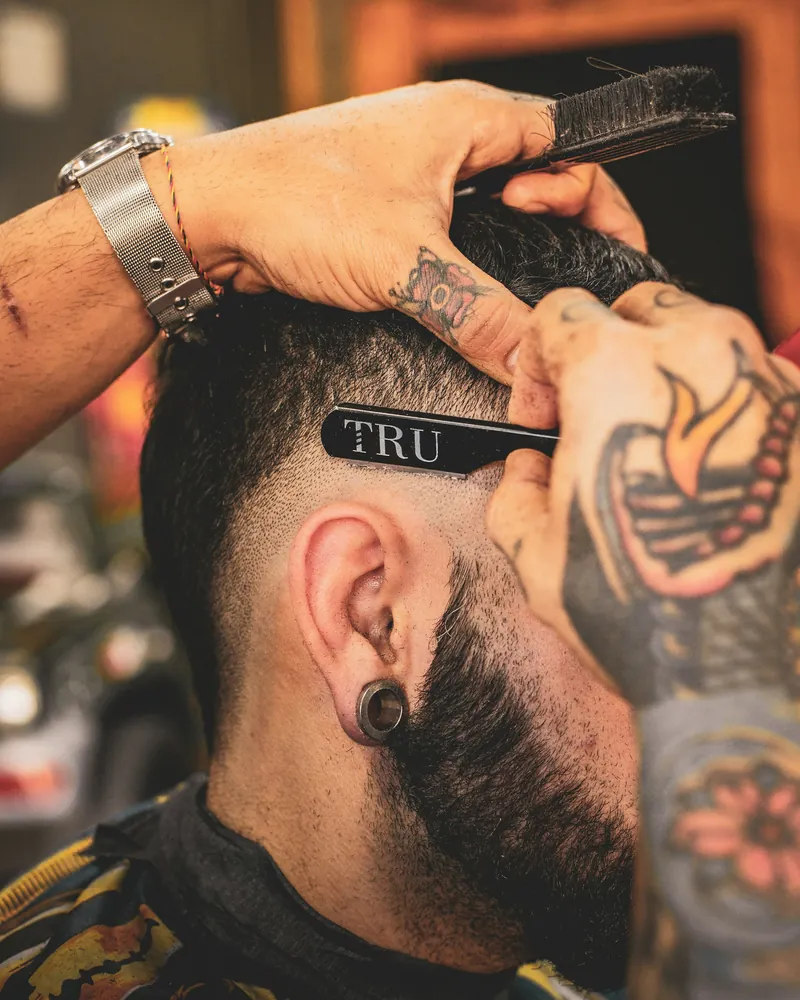 Tattooed barber lining up a fade with a straight razor