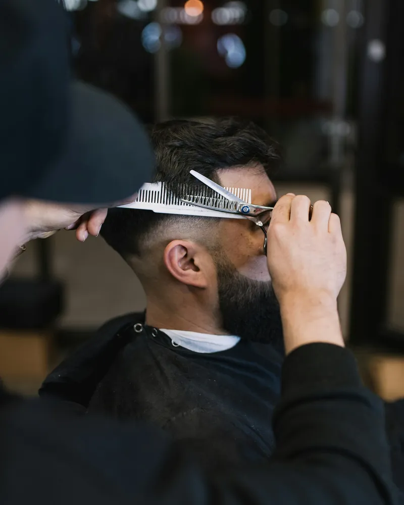Barber combing and scissor-cutting a client's hair over the comb
