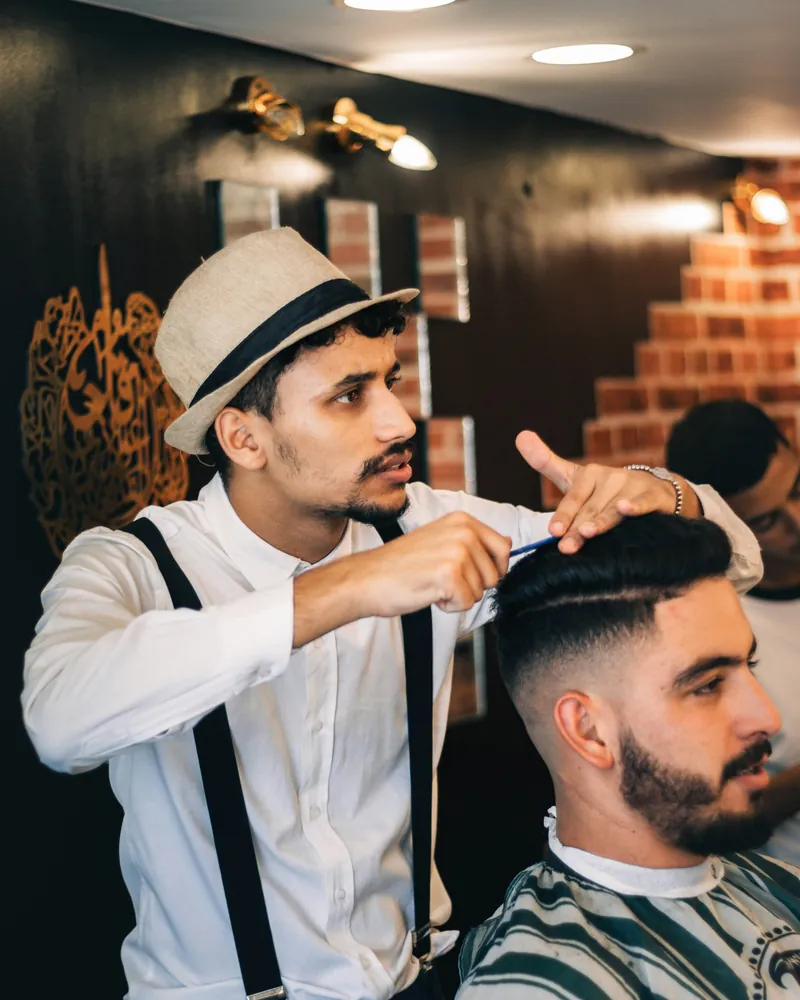 Barber in braces and a hat cutting a textured quiff