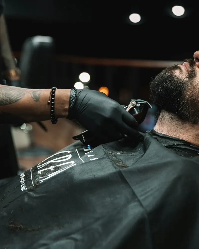 Barber in black gloves trimming a client's beard with clippers